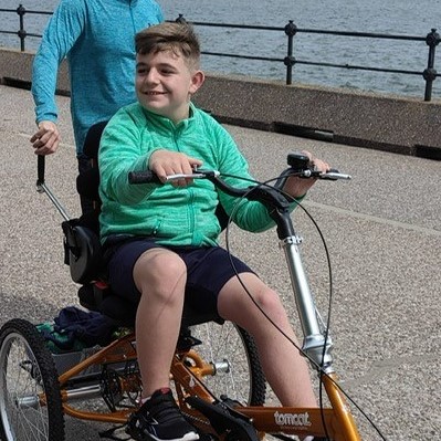 Cody riding on his adapted trike on the beachfront