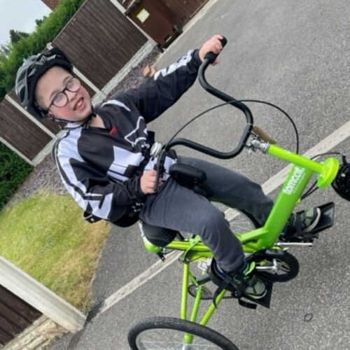 An 11-year-old boy is smiling on a green adapted trike